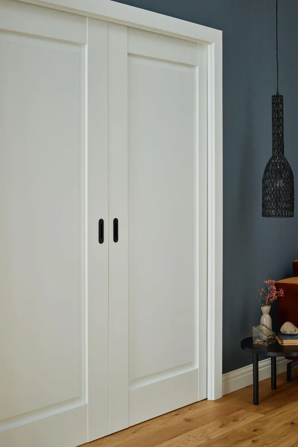 Białe drzwi przesuwne na tle ciemnej ściany w minimalistycznym wnętrzu.